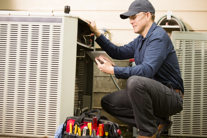 HVAC contractor using field service scheduling software on a tablet during a condenser service call